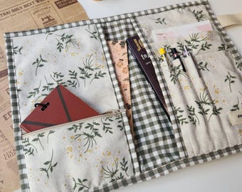 Könnte beinhalten: Offener Stoff-Organizer mit Blumen- und Vichy-Muster. Der Organizer hat mehrere Taschen mit einem Notizbuch, Stiften und einem kleinen Buch. Eine Reißverschlusstasche enthält ein rotes Notizbuch. Der Text "to" ist auf dem Buchrücken zu sehen.