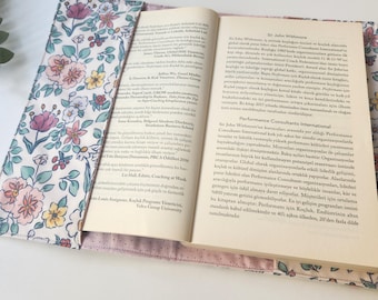 May include: Open book with a floral fabric cover. The cover features a pattern of pink, yellow, and purple flowers on a white background. The book is open to a page with text.