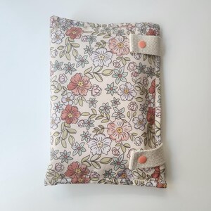 May include: A floral print changing pad cover with a cream background and a pattern of pink, white, and blue flowers. The cover has two cream-colored straps with peach-colored snaps.