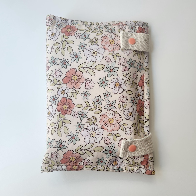 May include: A floral print changing pad cover with a cream background and a pattern of pink, white, and blue flowers. The cover has two cream-colored straps with peach-colored snaps.