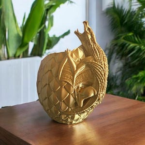 May include: A gold dragon sculpture emerging from a cracked golden egg. The dragon has its mouth open and its wings are spread out. The egg is textured and has a rough surface.
