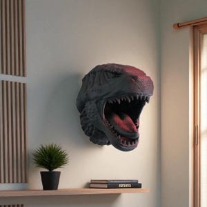 May include: A dark grey dinosaur head sculpture fixed to a wall, with an open mouth showing a red interior. The sculpture has detailed texture and sharp teeth. A small plant in a black pot sits on a shelf below.