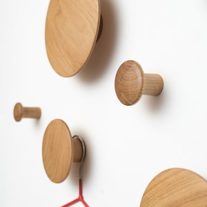 May include: Five wooden wall hooks shaped like mushrooms. The hooks are of different sizes and are mounted on a white wall.