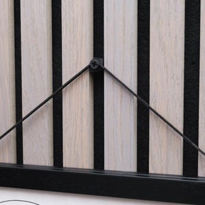 May include: Close-up of a wooden wall panel with vertical light-colored wood slats and black accents. The design includes black vertical stripes and a black frame. A black wire is attached to the panel.