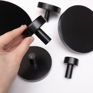 Op de afbeelding: Vijf zwarte ronde wandhaken met een houten knop. De haken zijn ontworpen om aan een muur te worden gemonteerd.