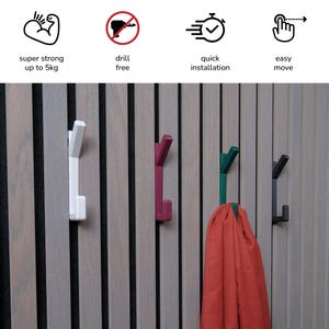 以下が含まれることがあります： 木製の壁に4つのフックが取り付けられています。フックは白、赤、緑、黒です。緑のフックに赤いスカーフがかけられています。