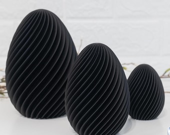 May include: Three black, egg-shaped decorative objects with a spiral design. The objects vary in size, with the largest in the back and the smallest in the front. The objects are on a white surface.