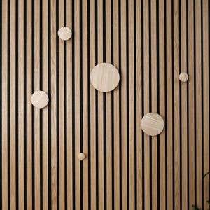 May include: A wall with vertical wooden slats in a light brown colour. There are five round wooden circles attached to the wall, each with a different diameter.