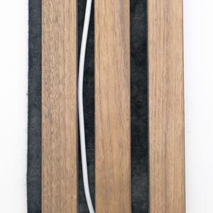 Peut inclure: Un panneau mural compos&eacute; de trois lattes de bois brun clair verticales fix&eacute;es sur un support en feutre gris fonc&eacute;. Un fin c&acirc;ble blanc passe verticalement entre la premi&egrave;re et la deuxi&egrave;me latte, cr&eacute;ant un contraste avec le feutre sombre.