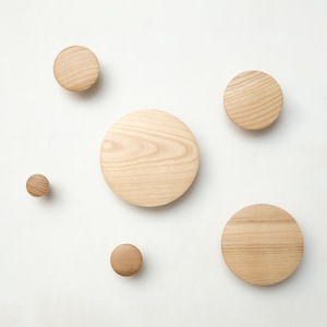 Può includere: Cinque ganci da parete in legno di diverse dimensioni, da piccoli a grandi, con una finitura in legno naturale. I ganci sono rotondi e hanno una superficie liscia.