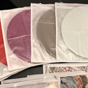 May include: Four round woven placemats in individual clear plastic bags. The placemats are red, purple, gray, and white.
