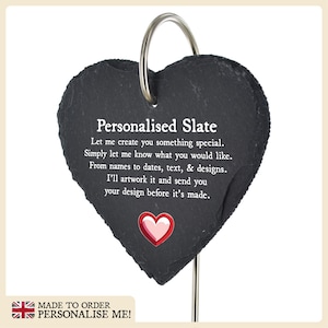 May include: A black heart-shaped slate plaque with a silver metal ring at the top. The plaque has white text that reads "Personalised Slate Let me create you something special. Simply let me know what you would like. From names to dates, text, & designs. I'll artwork it and send you your design before it's made." There is a small red heart with a white outline at the bottom of the plaque.