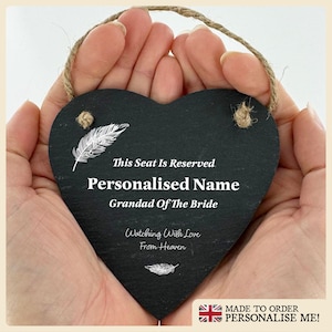 May include: Black heart-shaped slate sign with a white feather design. The sign reads "This Seat Is Reserved. Personalised Name Grandad Of The Bride Watching With Love From Heaven."
