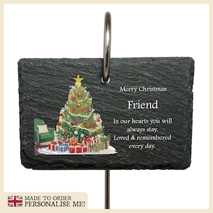 May include: A black slate Christmas memorial plaque with a colourful illustration of a Christmas tree and presents. The text reads "Merry Christmas Friend In our hearts you will always stay. Loved & remembered every day."