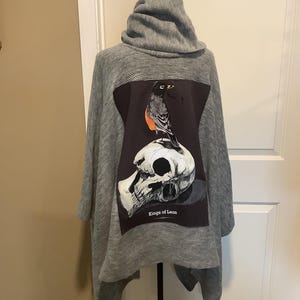 May include: Gray hooded sweater with a black and white graphic print of a bird perched on a skull. The graphic includes the text "Kings of Leon".