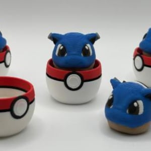 May include: Three blue and tan creature figurines with pointed ears and large eyes, each nestled inside a white, red, and black spherical container. One additional empty spherical container and one detached creature head are also present.