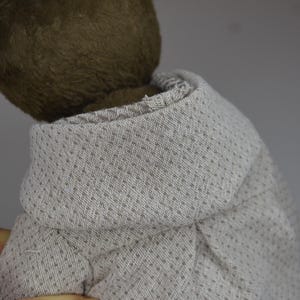 A close-up view of a teddy bear wearing a gray sweater with a patterned design.