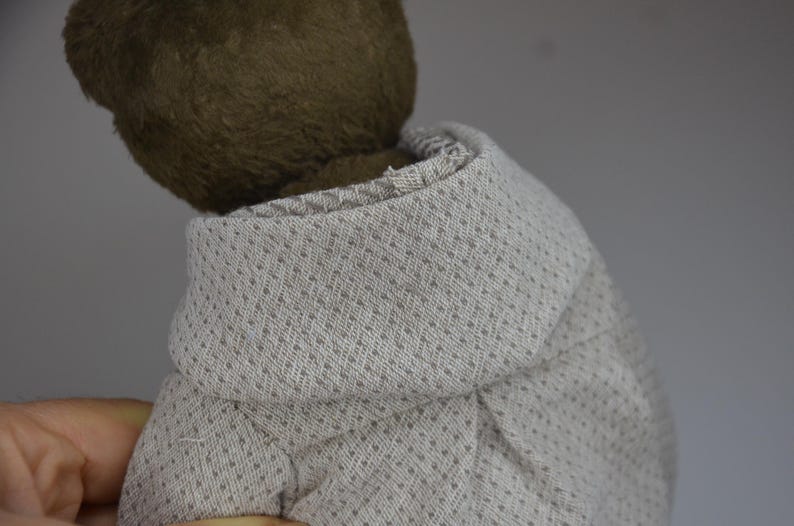 A close-up view of a teddy bear wearing a gray sweater with a patterned design.