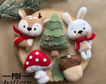 May include: A collection of handmade felt woodland ornaments, including a deer, rabbit, mushroom, acorn, and Christmas tree. The deer and rabbit wear red scarves. The ornaments are arranged on a wooden slice with the text "PDF pattern".