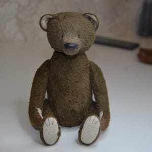 A brown teddy bear sitting on a white surface.