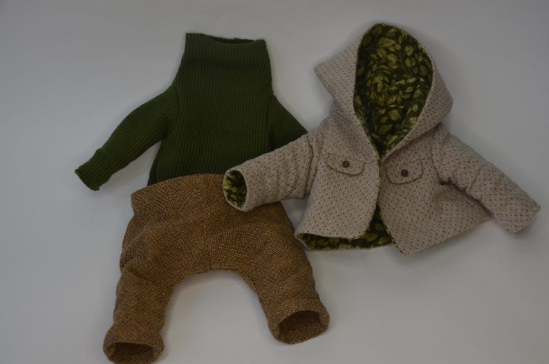 A green sweater and a beige jacket with a patterned lining are laid out on a white background.