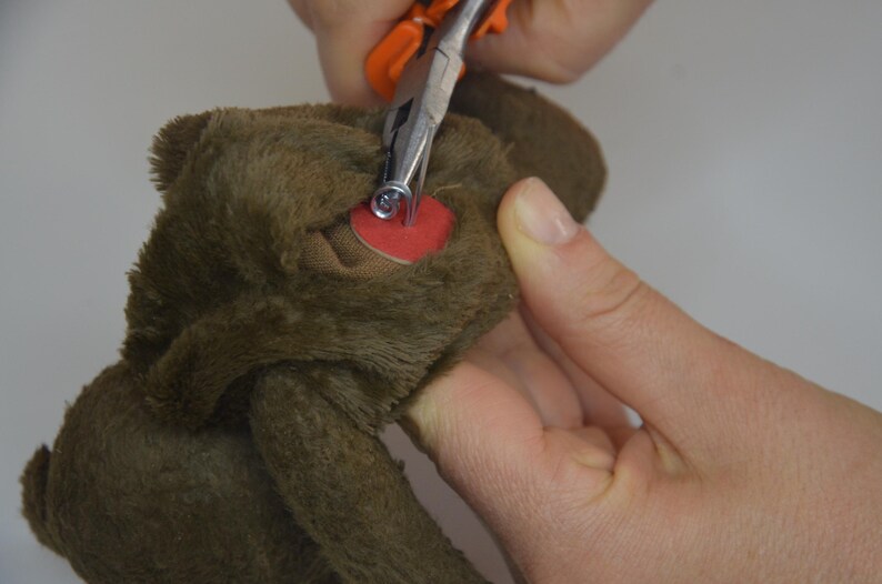 A person's hand is using a pair of scissors to cut the ear of a brown stuffed animal.