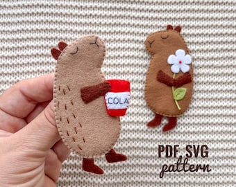May include: Two felt animal patterns for sewing, one holding a red cup with the word "COLA" on it, the other holding a white flower. The text "PDF SVG pattern" is below the animals.