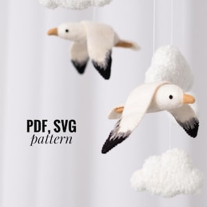 Puede incluir: Un móvil de fieltro con dos gaviotas blancas con detalles negros volando sobre nubes blancas y esponjosas. El texto "PDF, SVG pattern" está impreso debajo de las gaviotas.