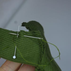 A hand holding a green fabric with a needle and thread, indicating some form of sewing or crafting activity.