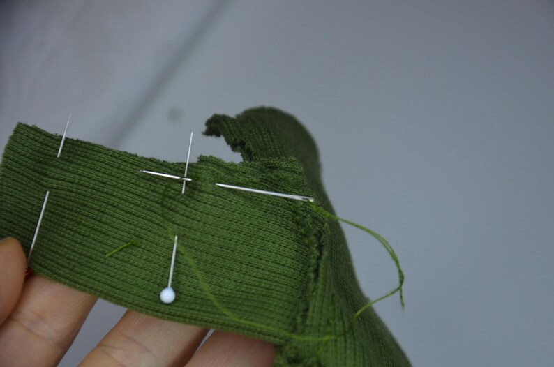 A hand holding a green fabric with a needle and thread, indicating some form of sewing or crafting activity.