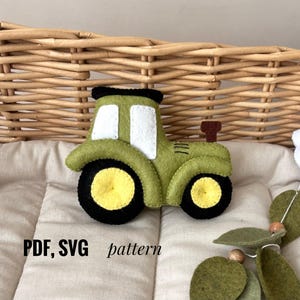 May include: A felt tractor in shades of green, black, and yellow. The tractor has white window details and a brown exhaust pipe. The text "PDF, SVG pattern" is visible in the lower left corner. The tractor is placed on a quilted surface.