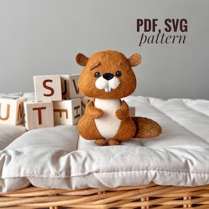 Pode incluir: Um brinquedo de castor de feltro marrom com barriga branca e uma cauda pequena. O brinquedo está sentado em um travesseiro branco com blocos de madeira atrás. O texto "PDF, SVG pattern" está escrito em marrom acima do brinquedo.