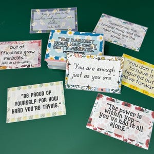 Peut inclure: Un ensemble de cartes d'affirmation color&eacute;es avec des motifs floraux et des citations inspirantes. Les cartes pr&eacute;sentent des citations telles que "L'heure la plus sombre ne dure que soixante minutes" et "Tu es assez tel que tu es."