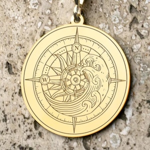 May include: Gold pendant necklace with a compass design featuring a wave and sun. The compass points north, south, east, and west.