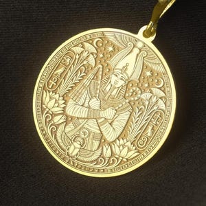 May include: A gold-toned circular pendant necklace featuring an intricate engraved design of an Egyptian pharaoh figure, lotus flowers, and various hieroglyphic symbols. The pendant hangs from a matching gold-toned metal chain link necklace.
