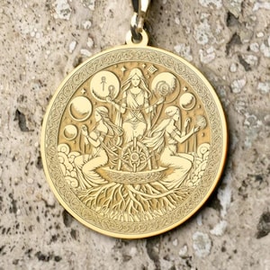 Puede incluir: Collar con colgante dorado. El colgante circular presenta un diseño grabado con tres figuras y otros símbolos. La cadena también es dorada. El colgante mide aproximadamente 3,8 cm de diámetro.