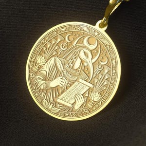 May include: A gold-toned circular pendant necklace featuring an engraved depiction of an ibis-headed figure holding a stylus and a scroll, surrounded by crescent moons and lotus flowers, suspended from a matching gold-toned link chain.