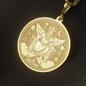 May include: A gold-toned circular pendant necklace featuring an intricate engraved design of a winged figure seated on a throne, surrounded by celestial symbols including stars, planets, and a crescent moon, suspended from a matching gold-toned chain.