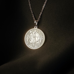 May include: A silver necklace with a round pendant featuring a detailed engraving of a woman standing in a forest with a crescent moon above her head.