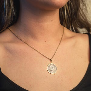 May include: A gold chain necklace with a round pendant featuring a detailed design. The pendant is silver and has a raised image of a person.