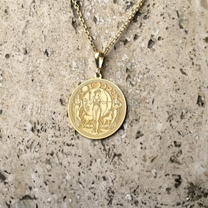May include: A gold necklace with a round pendant featuring a detailed engraving of a woman standing in a forest with a crescent moon above her head.