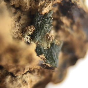 May include: Close-up of a green mineral formation embedded in a rough, brown rock. The mineral has a layered, crystalline structure.