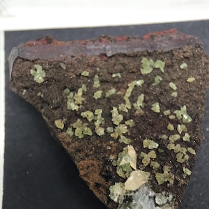 Op de afbeelding: Een close-up van een rots met groene en witte kristallen. De rots is bruin en heeft een ruwe textuur. De kristallen zijn klein en glinsteren.