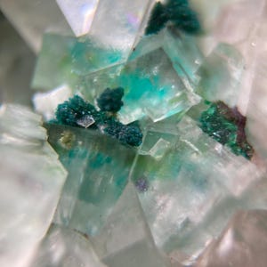 Puede incluir: Primer plano de un espécimen mineral con estructuras cristalinas translúcidas en tonos blancos, verde claro y turquesa. Se observan grupos de color verde oscuro dispersos, creando un contraste llamativo. La textura es áspera y angular.