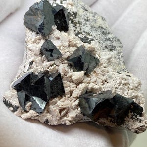 Puede incluir: Un grupo de cristales de magnetita negros octaédricos en una matriz blanca. Los cristales son afilados y bien formados, con un brillo metálico.