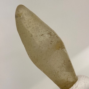 Peut inclure: Une pointe de cristal claire, facetée, de couleur brun clair avec une texture rugueuse. Le cristal est monté sur une base blanche.