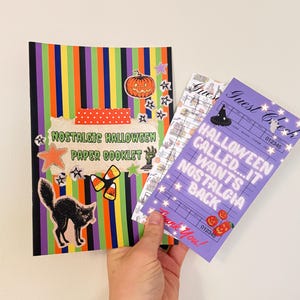 May include: A paper booklet with a vertical striped background in green, purple, orange, and black, featuring a pumpkin, candy corn, and black cat sticker. Beside it is a purple guest check card with the text Halloween Called...It Wants Nostalgia Back.