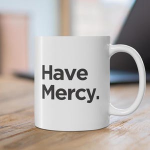 以下が含まれることがあります： 黒い文字で「Have Mercy.」と書かれた白いセラミック製のコーヒーカップ
