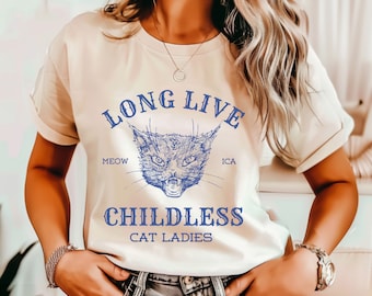 Op de afbeelding: Wit T-shirt met een blauwe afbeelding van een kattenkop en de tekst "Long Live Childless Cat Ladies" met de woorden "Meow" en "ICA" aan weerszijden van de kat.