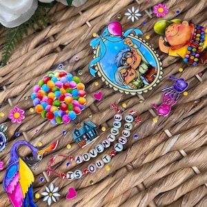 May include: A colorful Up themed resin tray with a house, balloons, a bird, a spider, and a couple in a frame. The tray also has a banner that says "Adventure is out there".